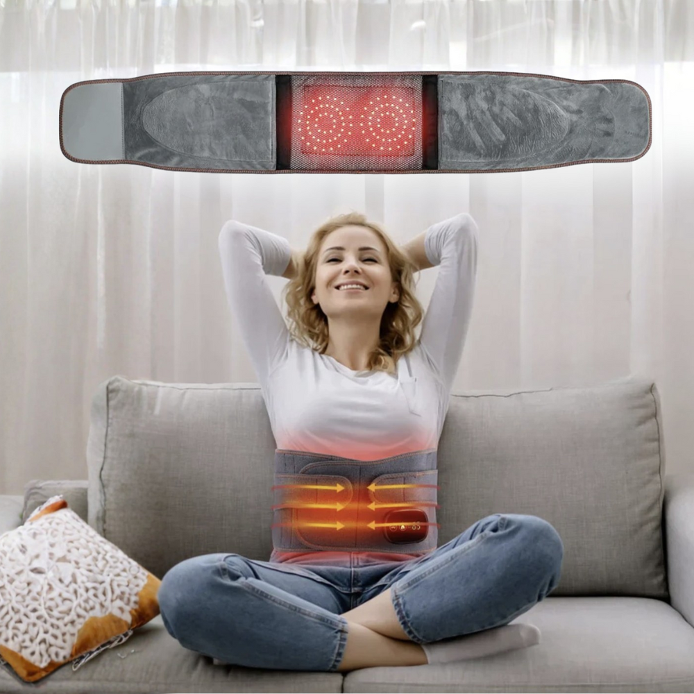 Woman sitting on a couch with an infrared massage and heating belt on her lap, showing glowing red and orange lights.